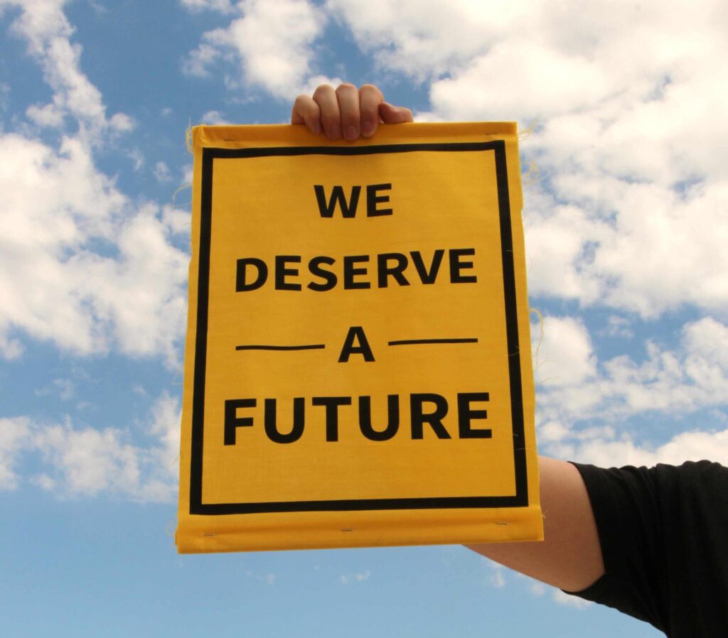 image of a person holding a sign that says "We deserve a future" with sky in the background